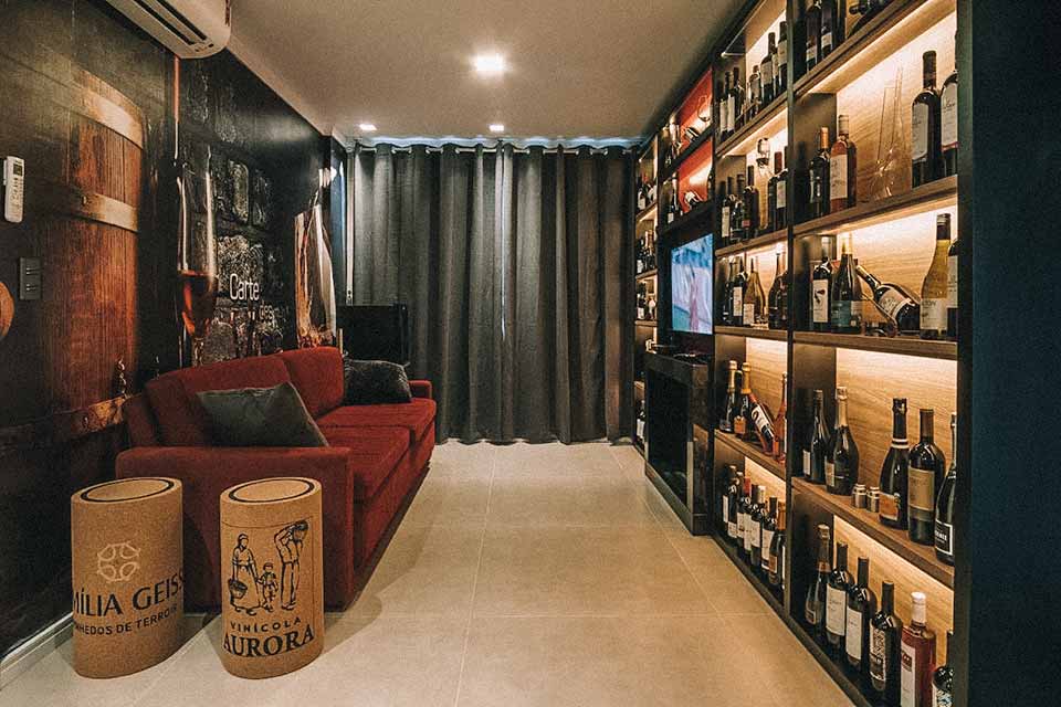 Sala de estar, com sofá vermelho e uma estante recheada de rótulos de vinho