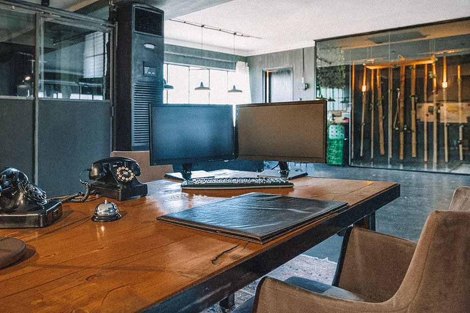 Sala de estar, com mesa de madeira com computadores, pastas e telefones em cima