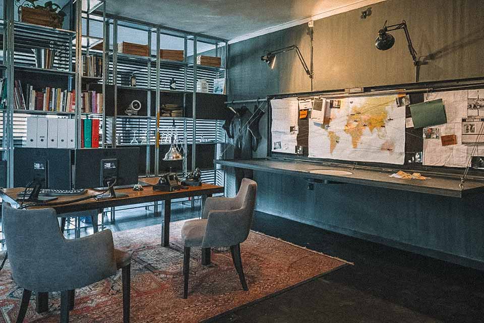 Sala de jantar, com mapa nas paredes, estantes de livros e mesa de 4 cadeiras